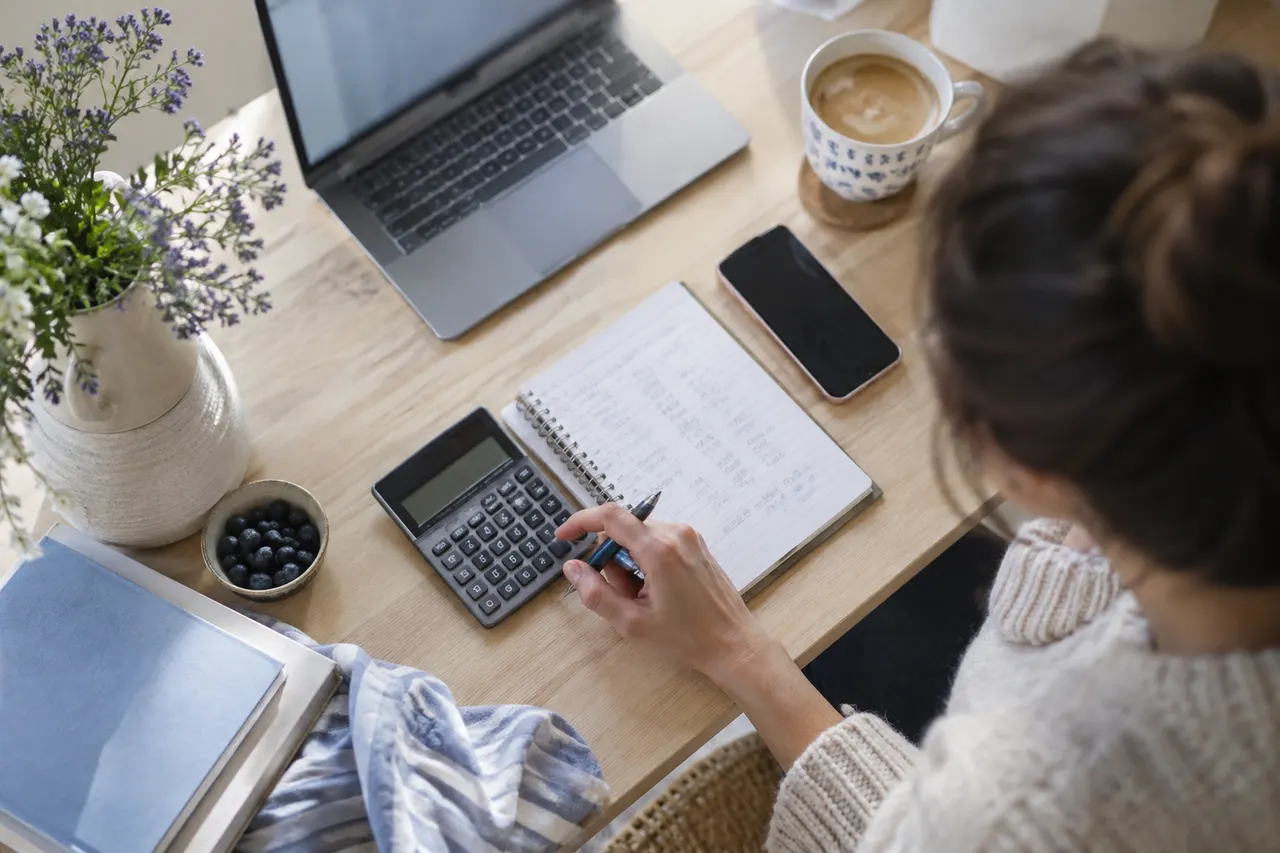 Overhead view of a desk with a calculator, notebook and phone mid-calculation